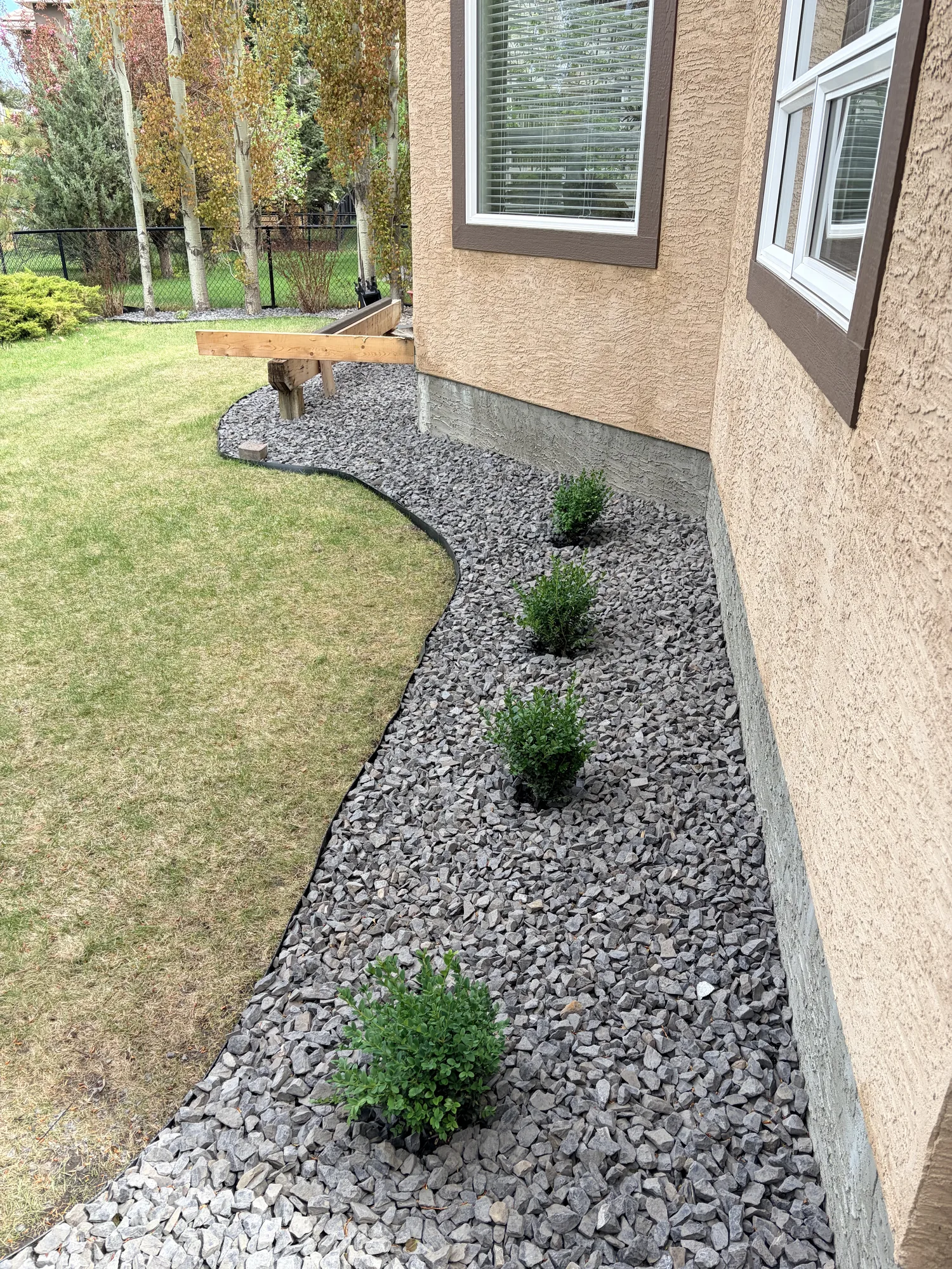 Decorative gray rock foundation bed with freshly planted shrubs along a Calgary home