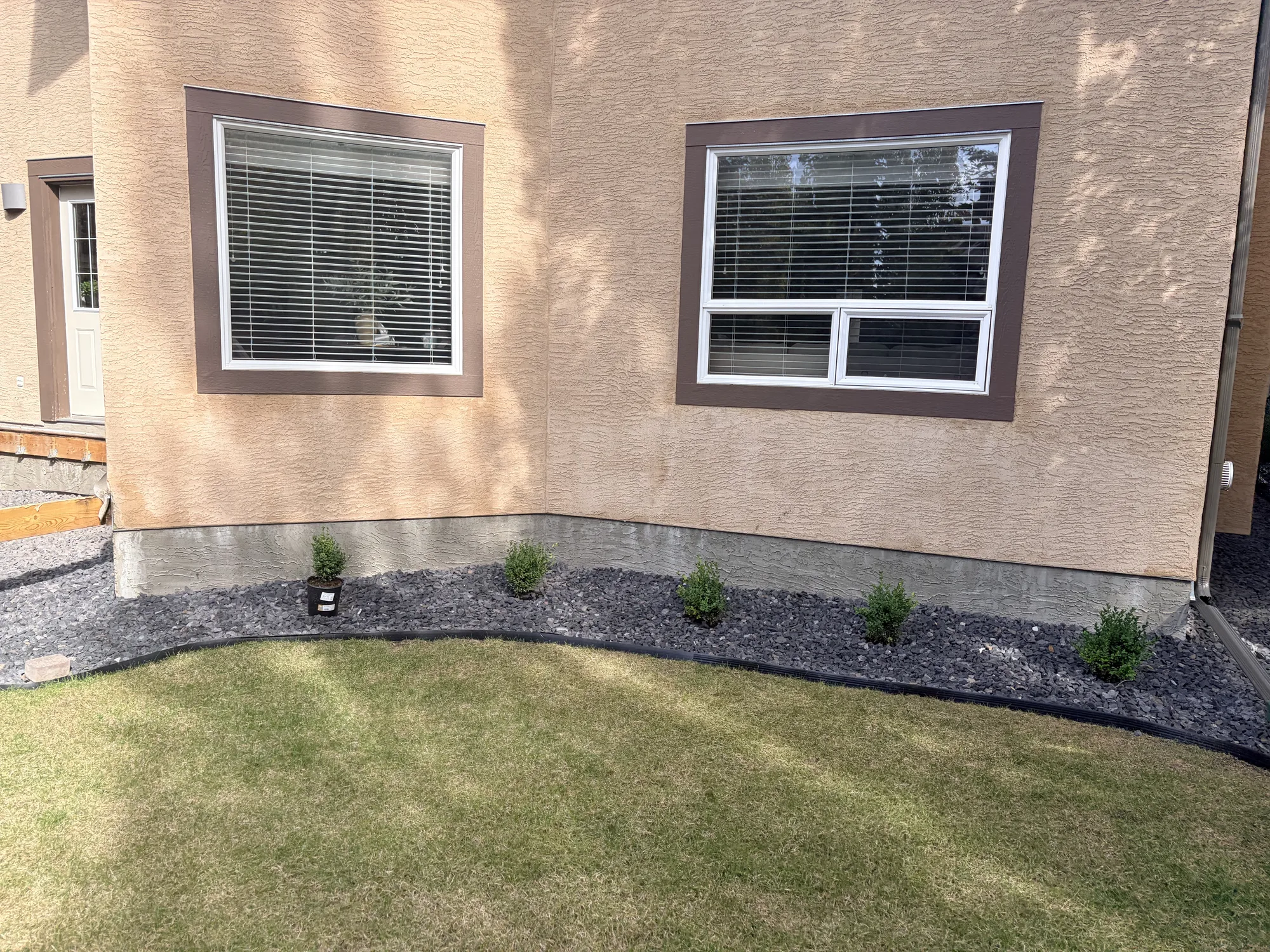 Decorative rock foundation bed with newly planted shrubs along a Calgary house