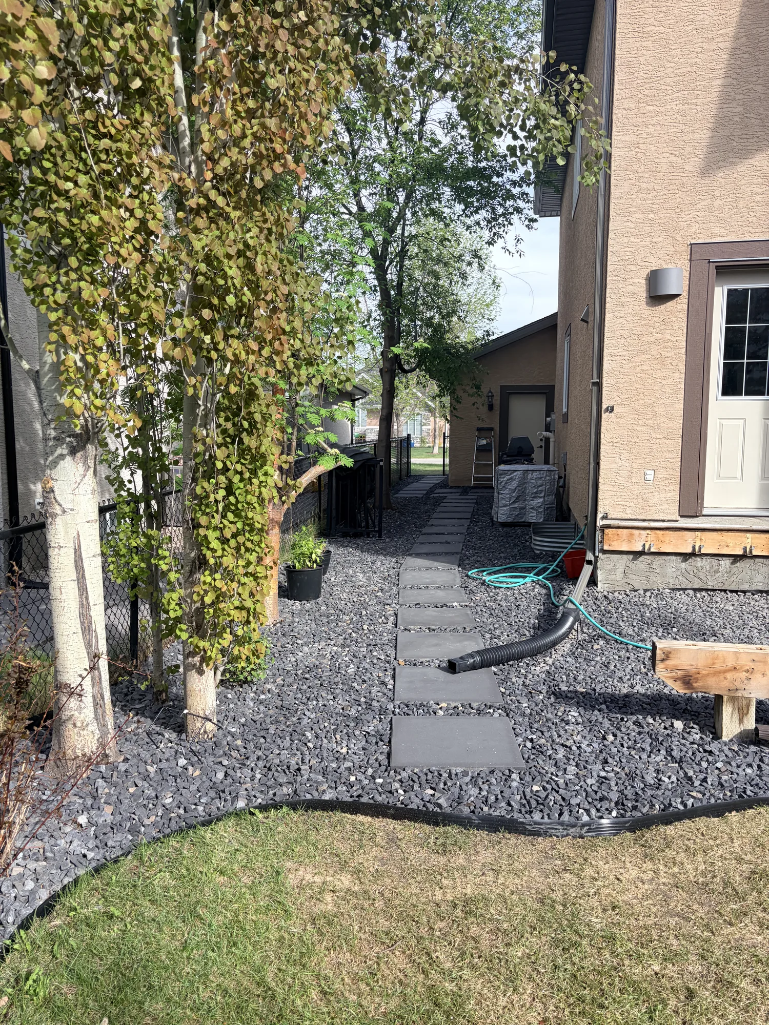 Side yard stepping stone path set in decorative rock with drainage between a Calgary home and fence