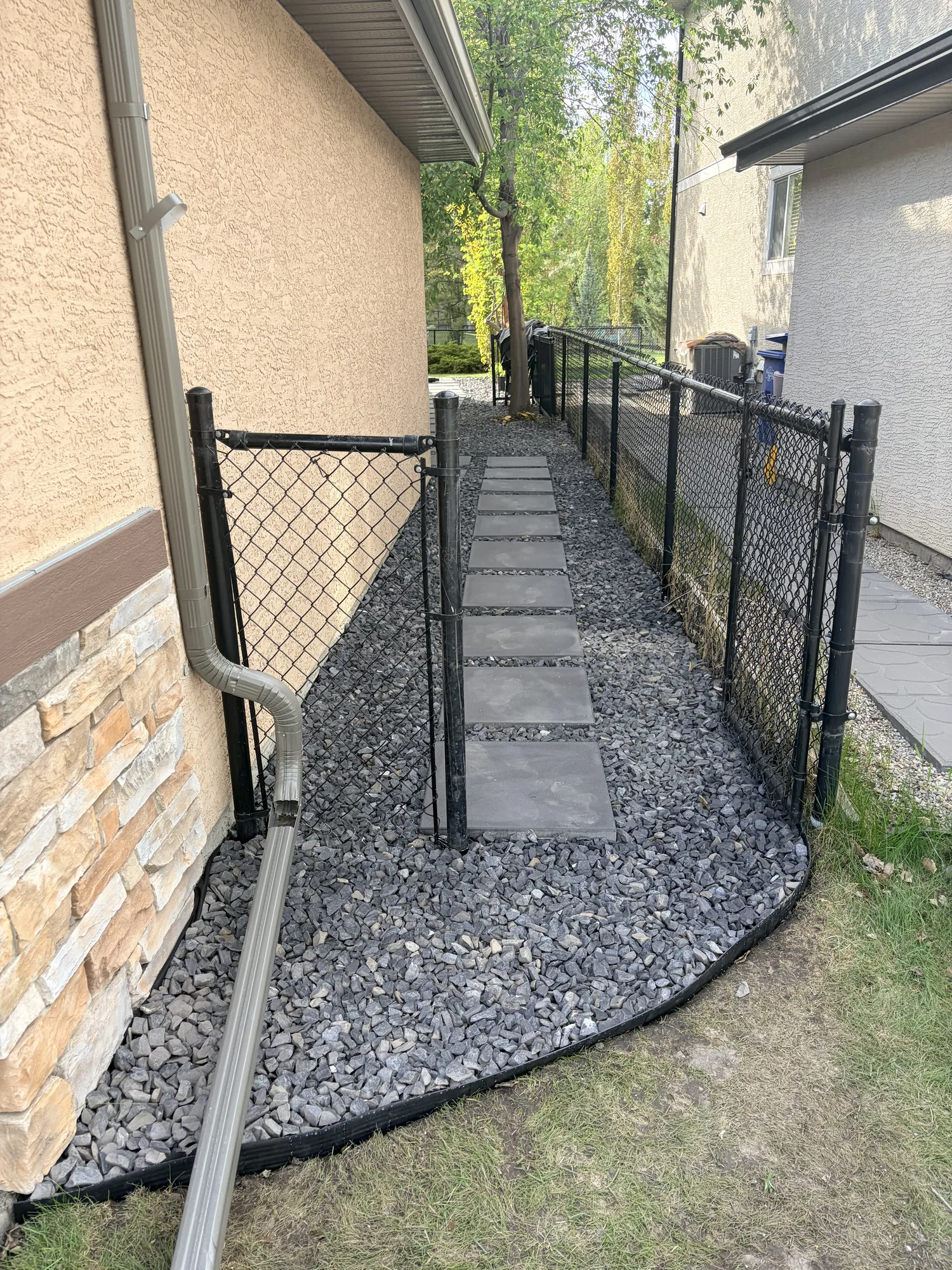 Side yard stepping stone pathway in decorative rock beside a Calgary home with a stone accent wall